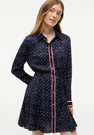 Woman wearing a navy blue long-sleeve dress with small red and white floral patterns and vertical striped button placket.