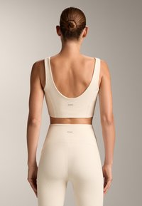 Helles beige Sport-Crop-Top und hochsitze Leggings aus strukturiertem Stoff, mit weitem Rundrücken und dezentem Logo am Bund.