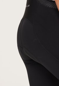 Zwarte sportlegging met een gestructureerde mesh tailleband, naadloos ontwerp en subtiele stiksels langs de contouren.