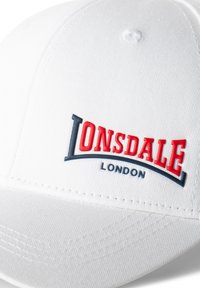 Bílá čepice s křivým kšiltem. Na přední straně se nachází 3D červené logo "LONSDALE" a modrý akcent. Vyrobena je z texturované tkaniny s viditelnými švy.