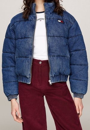 Osoba ubrana w niebieską pikowaną kurtkę dżinsową na białej koszulce Tommy Hilfiger, w połączeniu z wysokim stanem bordowych spodni ze sztruksu.