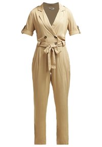 Combinaison beige à manches courtes avec col à revers, boutons croisés, manches retroussées et ceinture en tissu nouée à la taille.