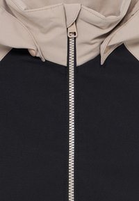 Close-up of a black and beige jacket with a central beige zipper and a partially folded hood.