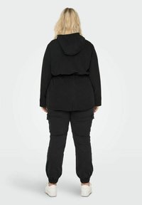 Juoda gobtuvinė striukė su prigludusia juosmena, derinama su suderintomis krovinių kelnėmis. Minkšta tekstūra ir elastinės rankogaliai, kelnėse yra šoninės kišenės.