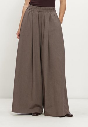 Pantalon marron à jambes larges avec une taille élastique, porté avec des chaussures foncées et un haut sans manches rentré, visible de la taille jusqu'aux pieds.