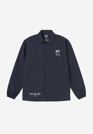 Veste boutonnée bleu marine avec col, poignets élastiques, poches avant, logo blanc de tasse de café dessin animé sur la poitrine gauche et texte près de l'ourlet inférieur.