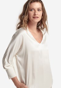 Top in satin bianco con scollatura a V e maniche lunghe con dettagli ai polsini. Texture liscia e taglio comodo per un indossare confortevole.