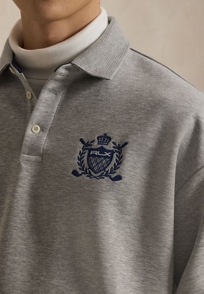 Γκρι πόλο μπλούζα με μικρό γιακά, που διαθέτει κεντημένο λογότυπο σε ναυτικό μπλε και λεπτομέρεια κορώνας. Κατασκευασμένη από υφασμάτινο μείγμα με λεία υφή.
