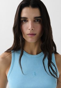 Lichtblauw geribbeld tanktop met een ronde hals. Met subtiele logodetails op de borst en een minimalistisch ontwerp. Zachte textuur.