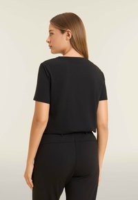 Camiseta negra de manga corta con escote redondo, textura suave y corte relajado, combinada con pantalones negros a juego.