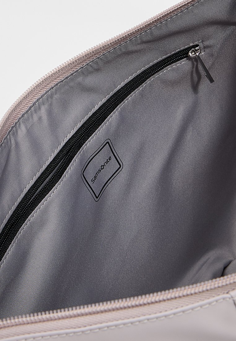 Grau gefüttertes Innenleben einer Tasche mit einem Reißverschlussfach und einem Etikett mit dem Markennamen "Samsonite". Die Außenseite ist hellrosa mit glatter Textur.