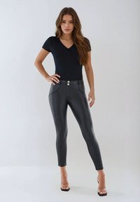 Svart figurnära bodysuit med korta ärmar kombinerad med högmidjade svarta byxor i konstläder med två metalliska knappar och framfickor.