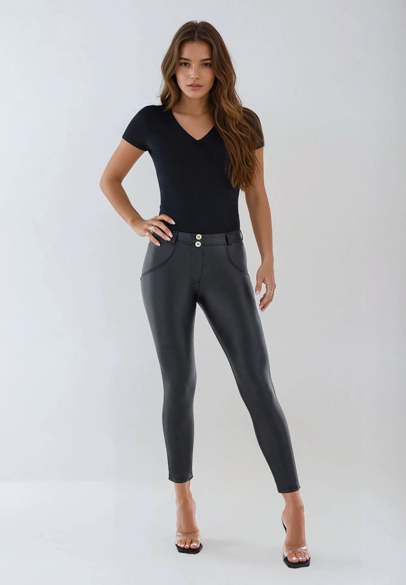 Svart figurnära bodysuit med korta ärmar kombinerad med högmidjade svarta byxor i konstläder med två metalliska knappar och framfickor.