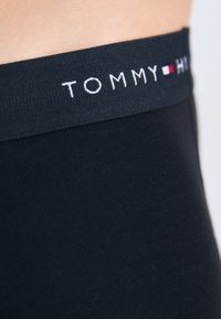 Fekete pamut boxer alsók sima felülettel és széles elasztikus derékrésszel, amelyen a "TOMMY HILFIGER" logó fehér és piros színben látható.
