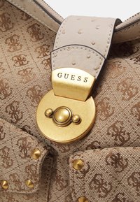 Borsa in tessuto marrone a motivo con chiusura in oro incisa "GUESS" e tracolla beige strutturata con cuciture e rivetti dorati.