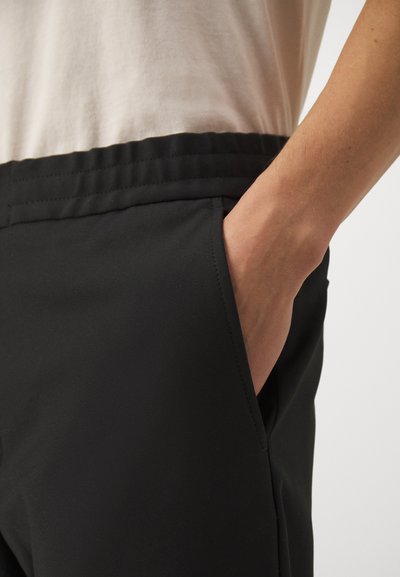 Mustad musta värvi treeningpüksid küljetaskutega, elastse vöökohaga ja sileda tekstiuriga. Tasku ääres on nähtav õmblusdetail.