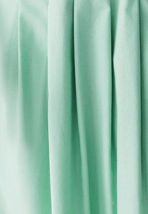 Tessuto plissettato di un morbido colore verde menta, caratterizzato da una texture liscia e pieghe verticali, che mostrano il riflesso della luce sulla superficie.