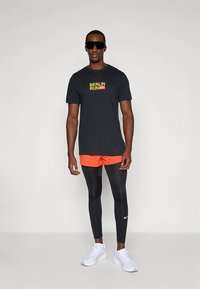 Must t-särk tekstiga "BERLIN RUN", oranžid püksid, mustad leggingsid ja valged tossud. Iseloomustab sile kangas ja tihe istuvus.