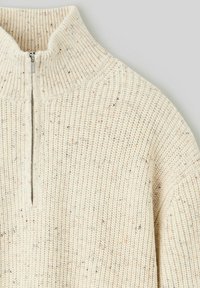 Pull en tricot de couleur crème avec un col montant et une fermeture éclair mi-hauteur. Motif texturé avec de subtils éclats de couleurs plus foncées.