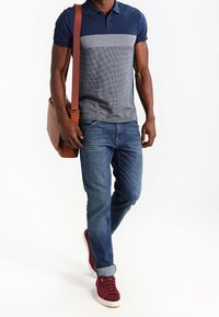 Granatowa i szara w paski koszulka polo, dżinsy, burgundowe trampki i brązowa skórzana torba na ramię.