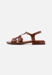 Sandales en cuir brun avec un design à bride en T, dotées d'accents brillants et de découpes florales courbées sur le dessus. Petit talon carré.