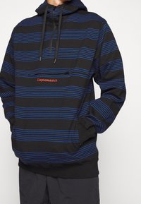 Felpa con cappuccio nera con strisce orizzontali blu, dotata di tasca con zip e logo rosso "Clevtomanicx" sul petto. Cappuccio con coulisse incluso.