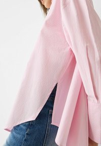 Rosa och vitrandig skjorta med lös passform, långa ärmar, sidofickor och en slät textur, bärs över blå denimjeans.