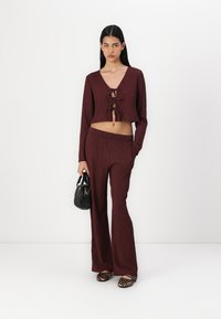 Burgundy two-piece set with a cropped, tie-front long-sleeve top and high-waisted, wide-leg pants. Textured fabric and animal print footwear.