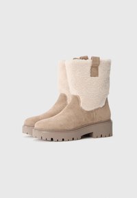 Tan suède enkellaarsjes met een fluffy crème schapenwollen rand, voorzien van een dikke profielzool en een trekloepje voor gemakkelijk aan- en uittrekken.