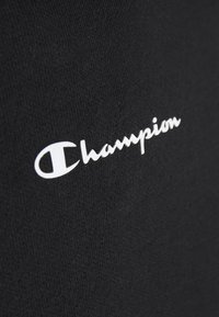 Tessuto nero con il logo "Champion" stampato in un carattere corsivo vicino al centro.