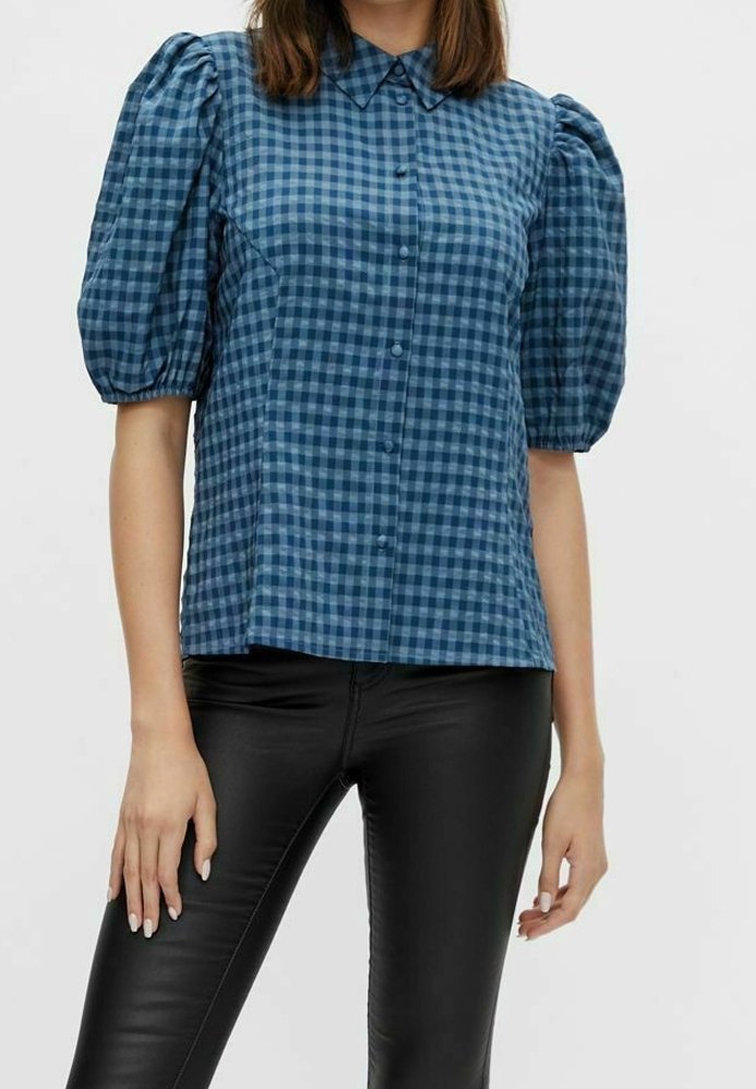 Blusa a maniche puff a quadri blu con chiusura a bottoni, colletto e vestibilità rilassata, abbinata a pantaloni in pelle nera.