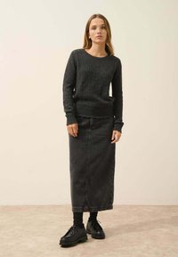 Tmavě šedý pletený svetr s texturovaným vzorem, v kombinaci s dlouhou šedou denimovou sukní a černými šněrovacími botami, stojící na neutrálním pozadí.