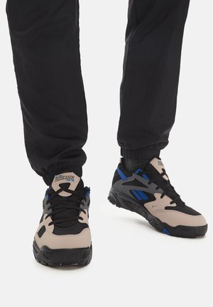 Beżowe i czarne sneakersy z niebieskimi akcentami, wykonane z teksturowanego materiału, zawiązywane na sznurówki i wyposażone w wytrzymałą gumową podeszwę.