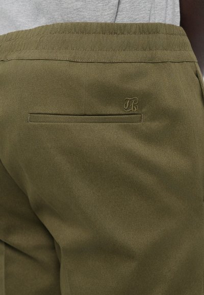 Olivenfarvede bukser med en tekstureret stof. Har en baglomme og en subtil broderet logo nær taljen. Elastisk taljedesign.