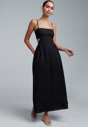 Black maxi dress with a fitted bodice, thin straps, side cutouts, and a flowing skirt. Made from lightweight fabric, features minimal accents.