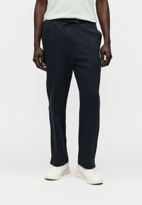 Σκούρες μπλε φόρμες από μαλακό ύφασμα, με κορδόνι στη μέση, πλευρικές ραφές και λογότυπο στην αριστερή μηρό.