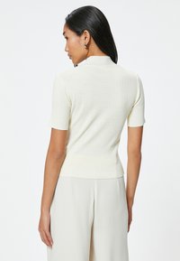 Top de manga corta en crema con diseño ajustado y cuello alto. Textura suave y tela ligeramente elástica. Estilo simple y versátil.