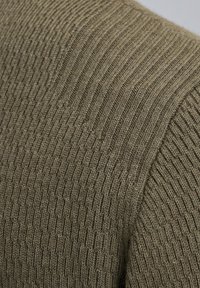 Olivgrüner, gestrickter Pullover mit gerippter Textur, markanten Linien und weichem Finish, das sein leichtes und atmungsaktives Design betont.