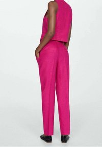 Ensemble en lin rose composé d'un haut sans manches et de pantalons droits avec poches latérales. Le tissu présente une finition légèrement texturée.