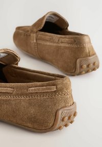 Braune Wildlederschlüpfschuhe mit weicher Textur, ausgestattet mit einer Gummisohle und kleinen Grip-Punkten an der Ferse für besseren Halt.