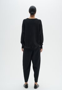 Pull noir surdimensionné avec poignets côtelés, associé à un pantalon noir ample. Texture lisse, design minimaliste, sans accents remarquables.