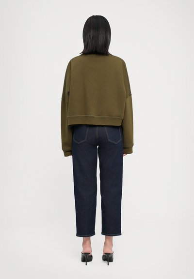 Felpa verde oliva a girocollo con spalle scese, abbinata a jeans dritti blu scuro e sandali con tacco neri.