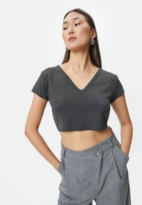 Kulkulsort cropped t-shirt med V-hals og korte ærmer, lavet af blødt stof, kombineret med lysegrå high-waisted bukser.