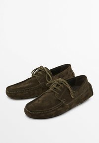 Scarpe da barca in suede marrone con lacci sul davanti, morbida texture, cuciture in stile mocassino e design della punta arrotondata.