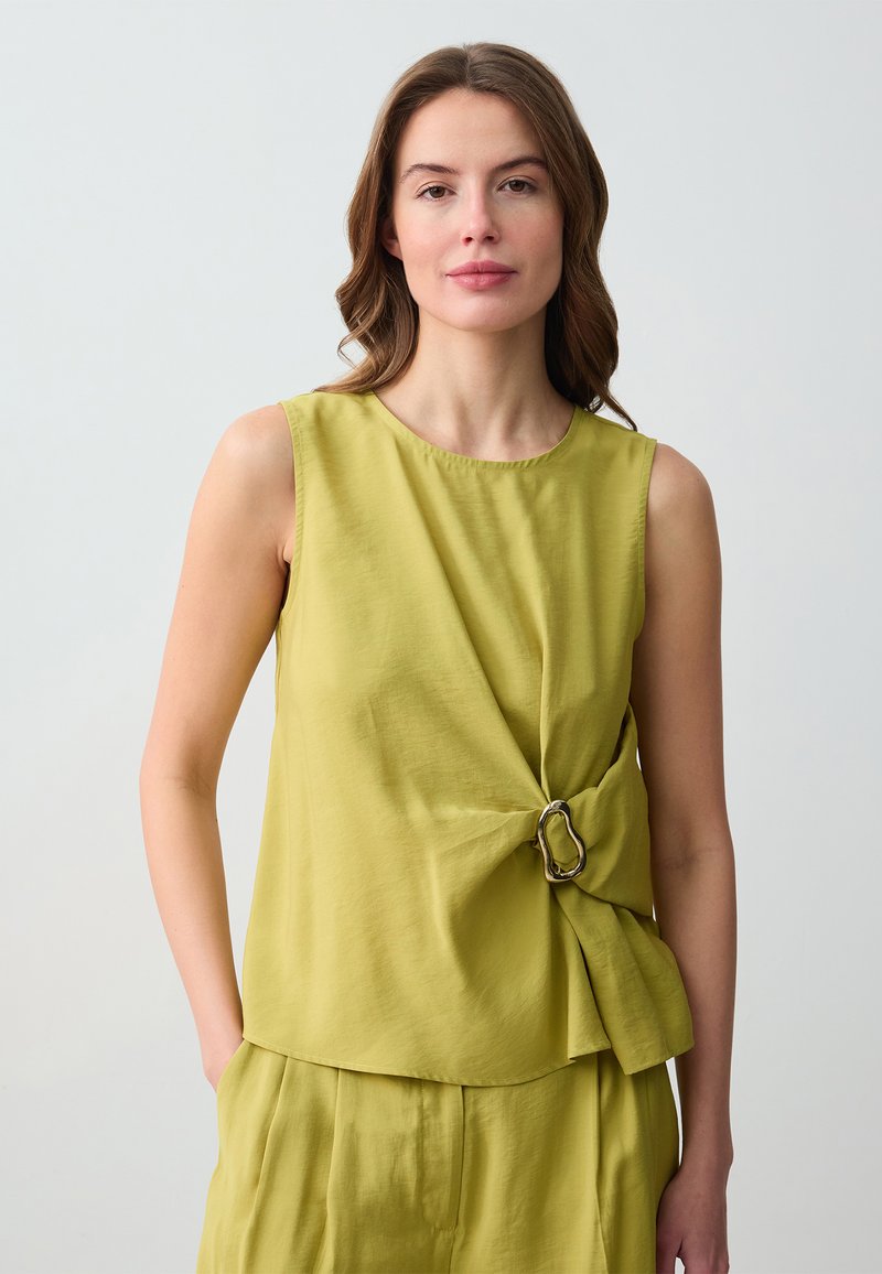 Top senza maniche verde con un design intrecciato e dettagli in metallo argentato. Tessuto liscio; vestibilità comoda. Abbinato a pantaloni coordinati.