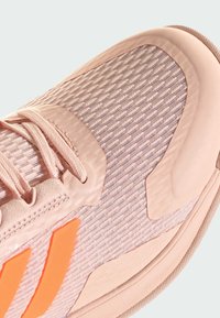 Detailný záber na ružovú textúrovanú tenisku s látkovým zvrškom, tónovými šnúrkami a oranžovými akcentmi na boku.