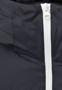 Veste noire avec une fermeture éclair blanche, matériau léger et surface texturée avec des coutures apparentes le long des coutures.