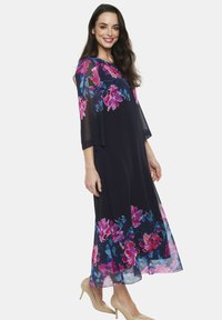 Maxi sukienka w granatowym kolorze z kwiatowym nadrukiem w odcieniach różu, fioletu i niebieskiego. Przezroczyste rękawy i lekki materiał. Beżowe szpilki dopełniają całość.