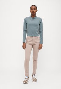 Top de manga larga azul claro con cuello redondo, emparejado con jeans ajustados beige y zapatillas blancas con detalles marrones. Conjunto simple y casual.