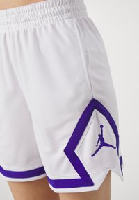 Balti sportiniai šortai su tinklinio tekstūra, violetiniais akcentais ir išskirtiniu violetiniu deimanto formos logotipu su ikonine siluetu.